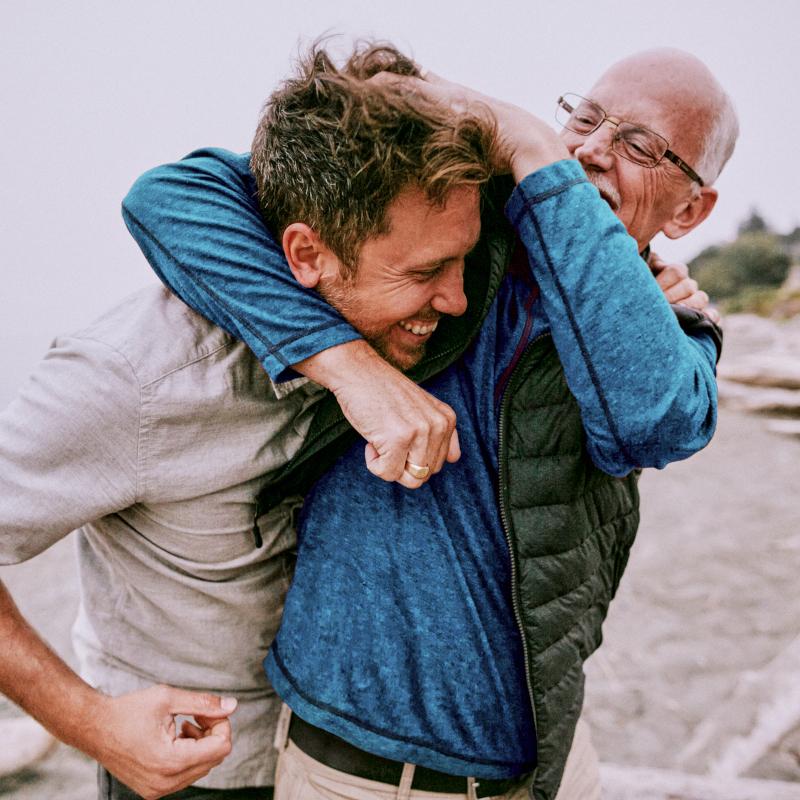 A happy senior man playfully hugs and rubs a man his head on the beach