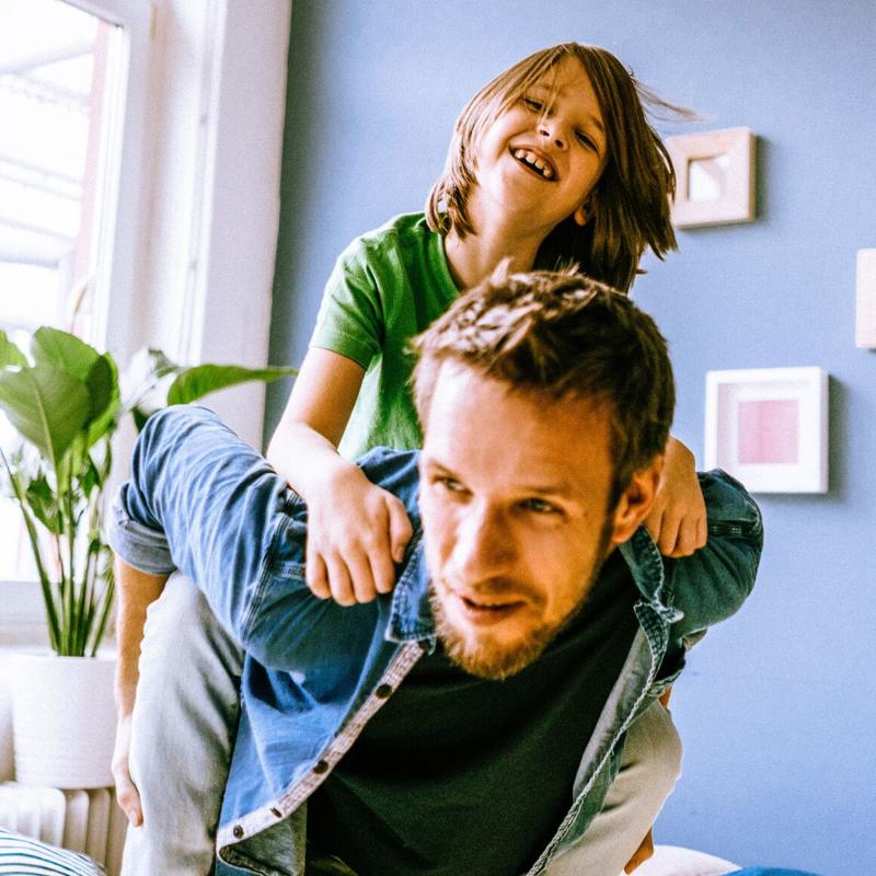 A man gives a happy young boy a piggy back ride at home in the living room
