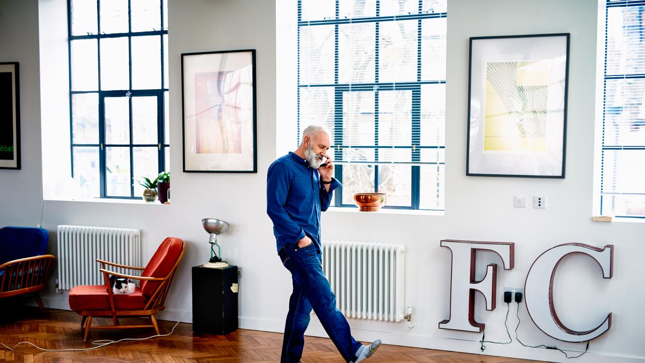 A man on the phone walks around the office with his hand in his pocket