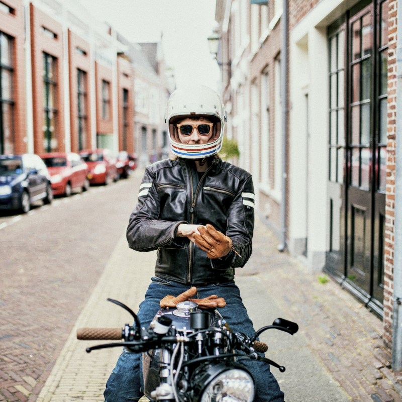 A young man wearing a helmet and a leather jacket sits on his motorbike 800x800