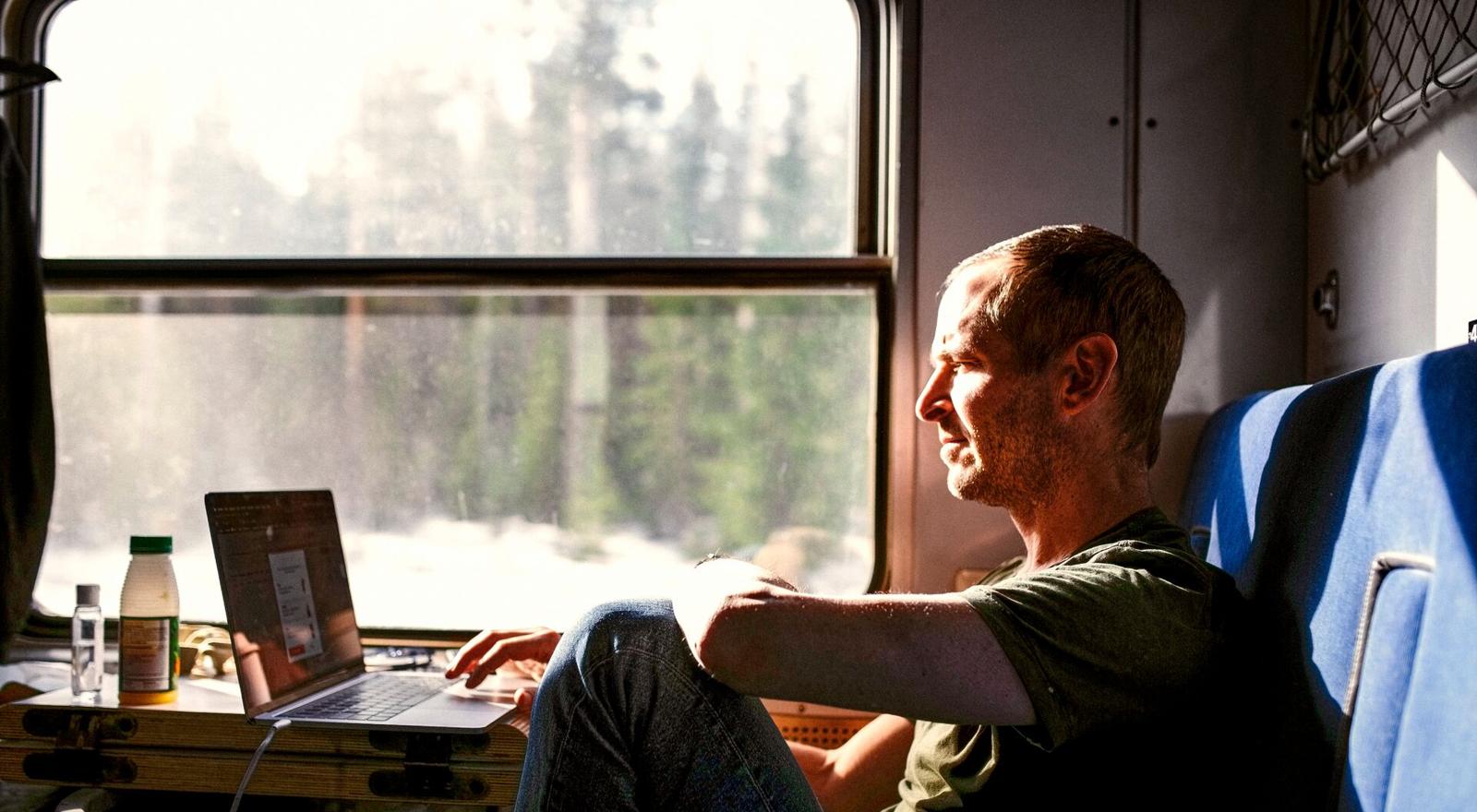Large Web and Screen A man using his laptop while sitting on a train in the sunlight