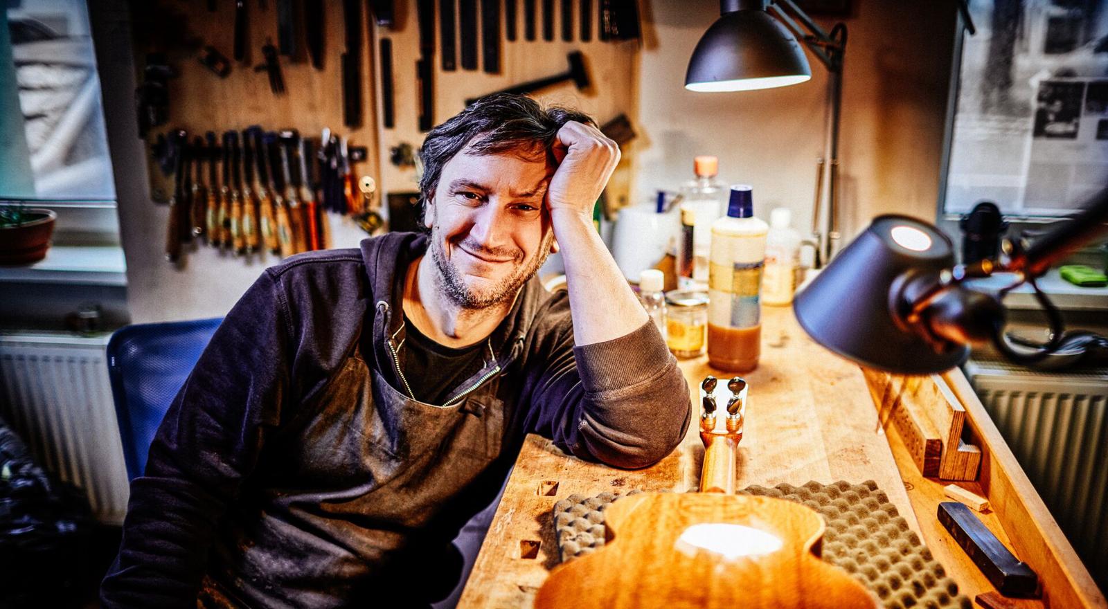 Large Web and Screen A smiling craftsman is fixing a guitar in a repair workshop