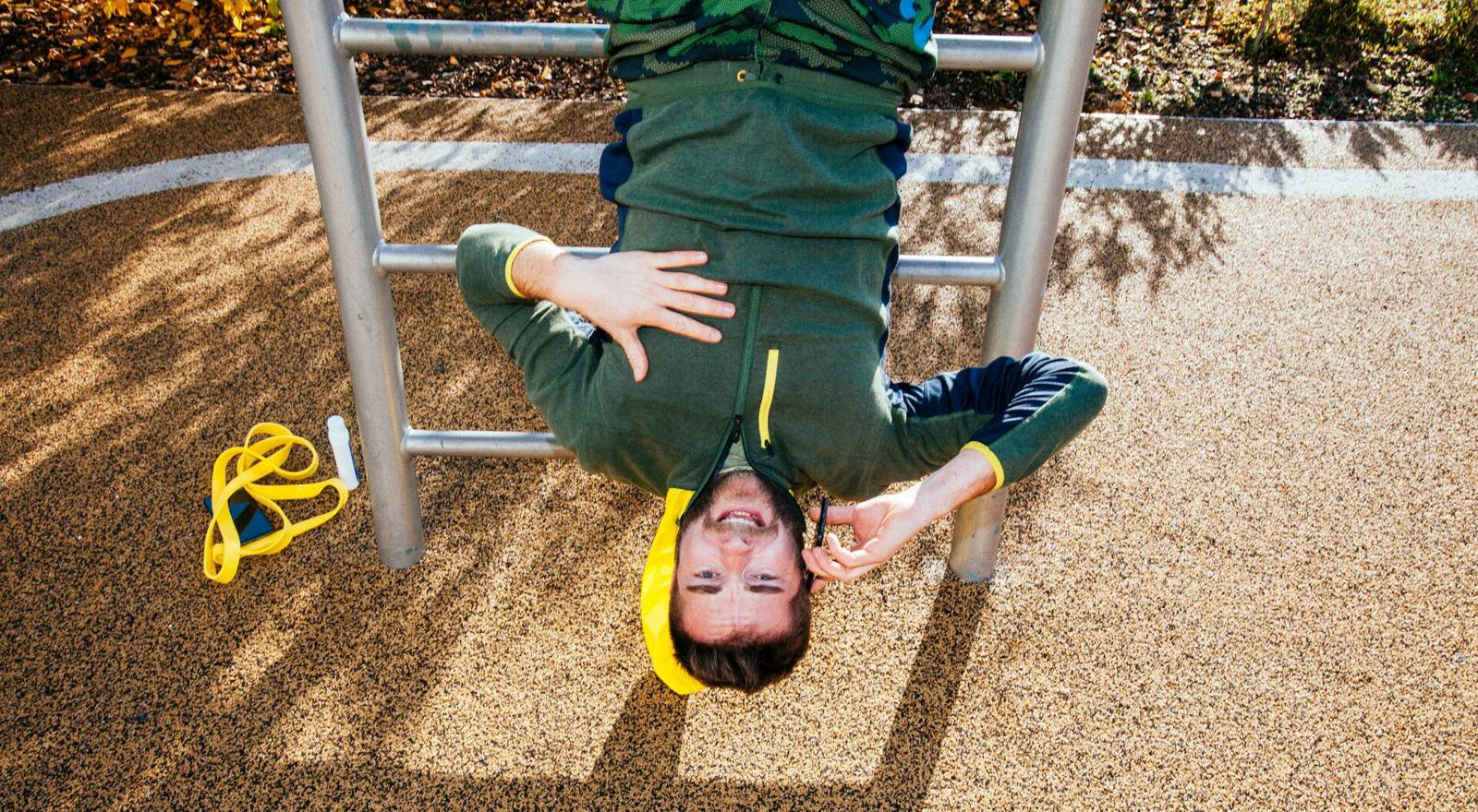Large Web and Screen A young man is talking on the phone while hanging upside down from an outdoor gym equipment