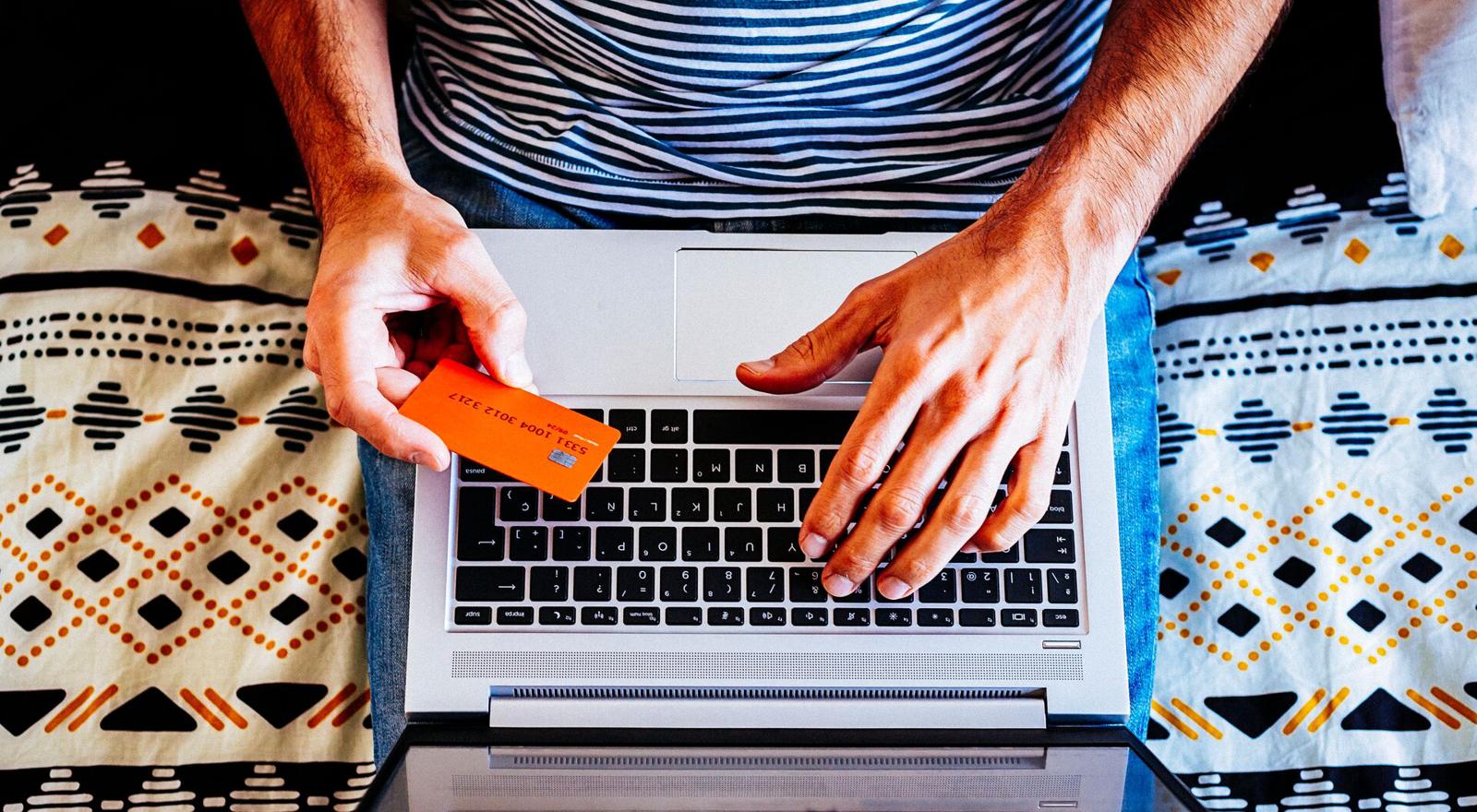 Large Web and Screen Overhead view of man sitting with his laptop on his lap and his bank card in his hand