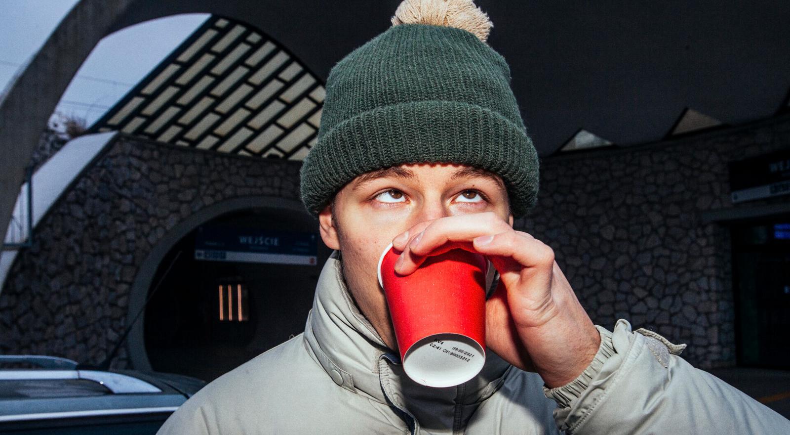 Large Web and Screen Young man in a wool hat looking up while drinking from a paper cup outside