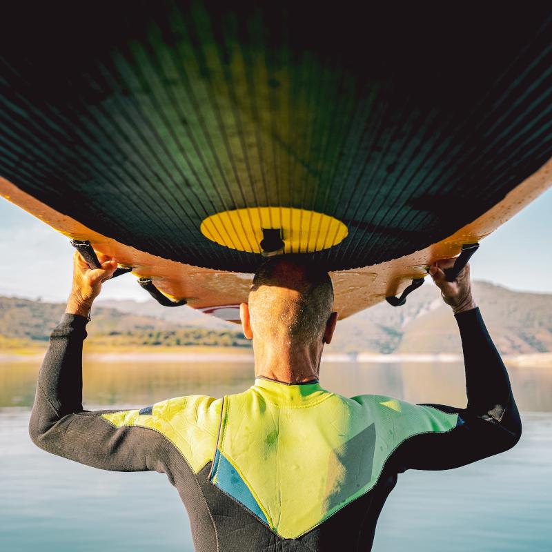 Rear view of man holding surf board above head