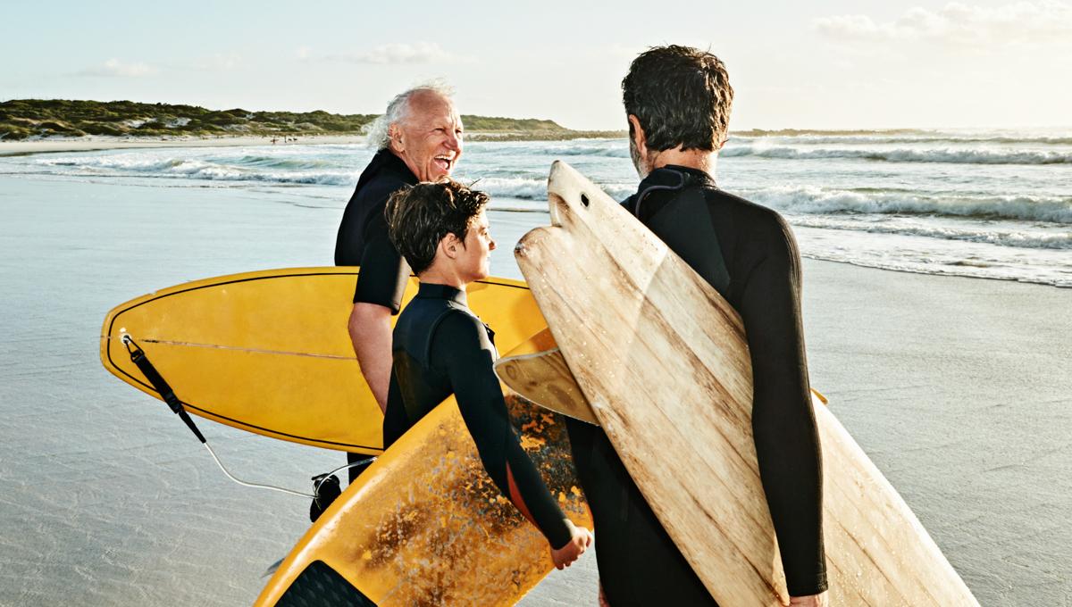 Three people in wetsuits stand in the sea with their surfboards 1200x680